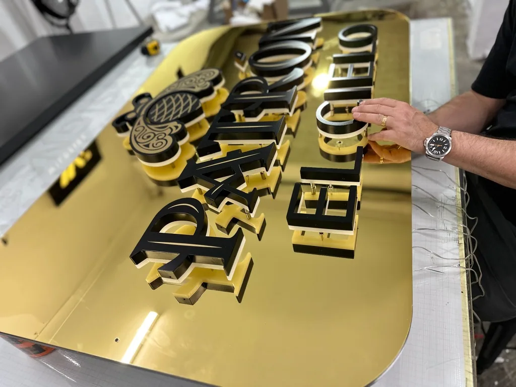 Illuminated Patron 3D letters being assembled on a gold sign panel