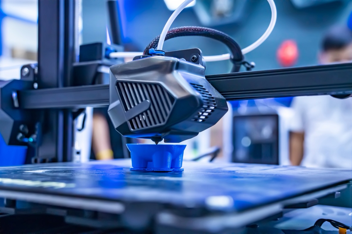 FDM print head building a blue polymer part layer by layer on the print bed