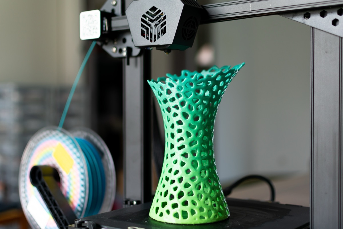 Green lattice vase form standing finished on the printer build plate beside the filament spool