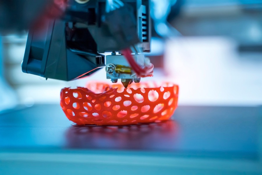 FDM print head extruding a red lattice part on the build plate during a 3D print