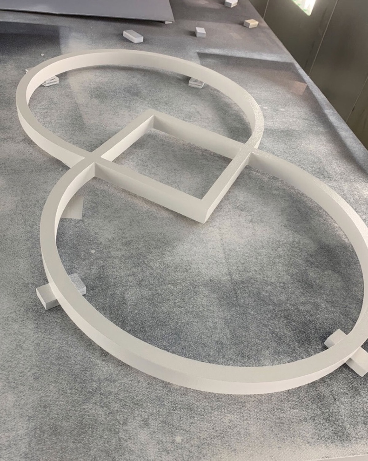 Large routed logo profile of interlocking rings and a diamond, freshly coated white on the finishing table
