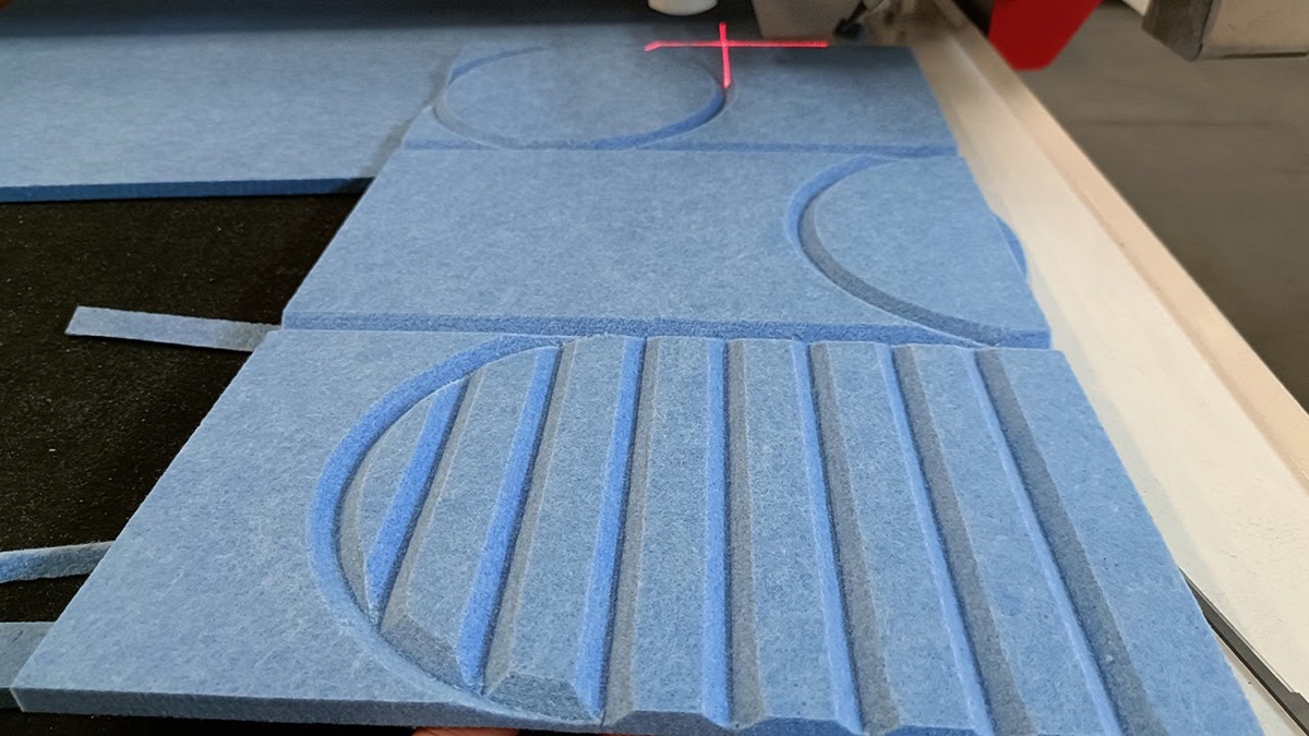 Blue acoustic felt tiles with grooved circle and line patterns on the cutter bed under the registration laser