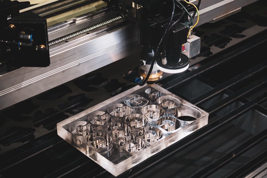 CO2 laser head cutting nested letterforms from a thick clear acrylic sheet