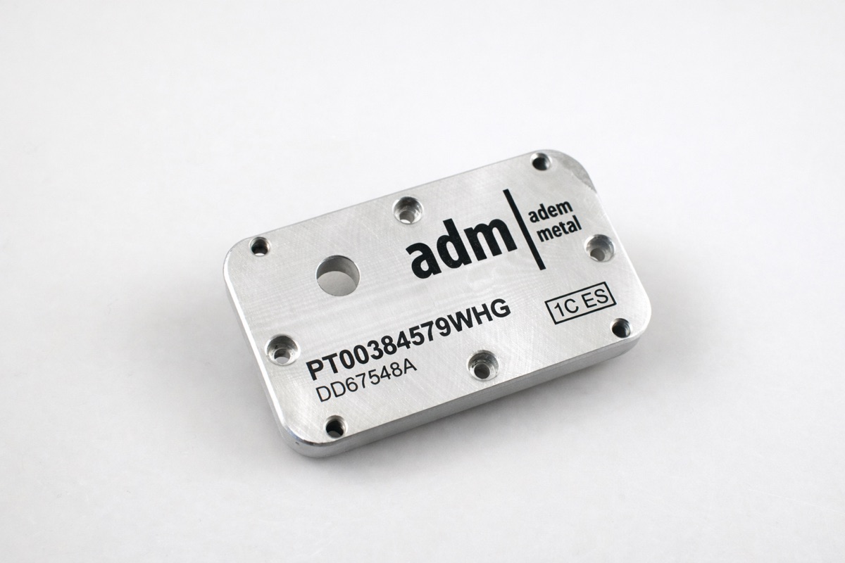 Machined aluminium block marked with logo and part numbers