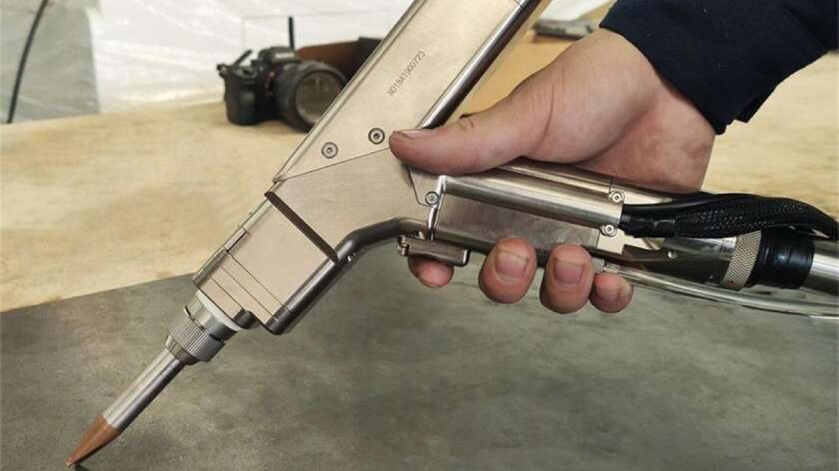 Operator holding a handheld fiber laser welding gun above the workbench