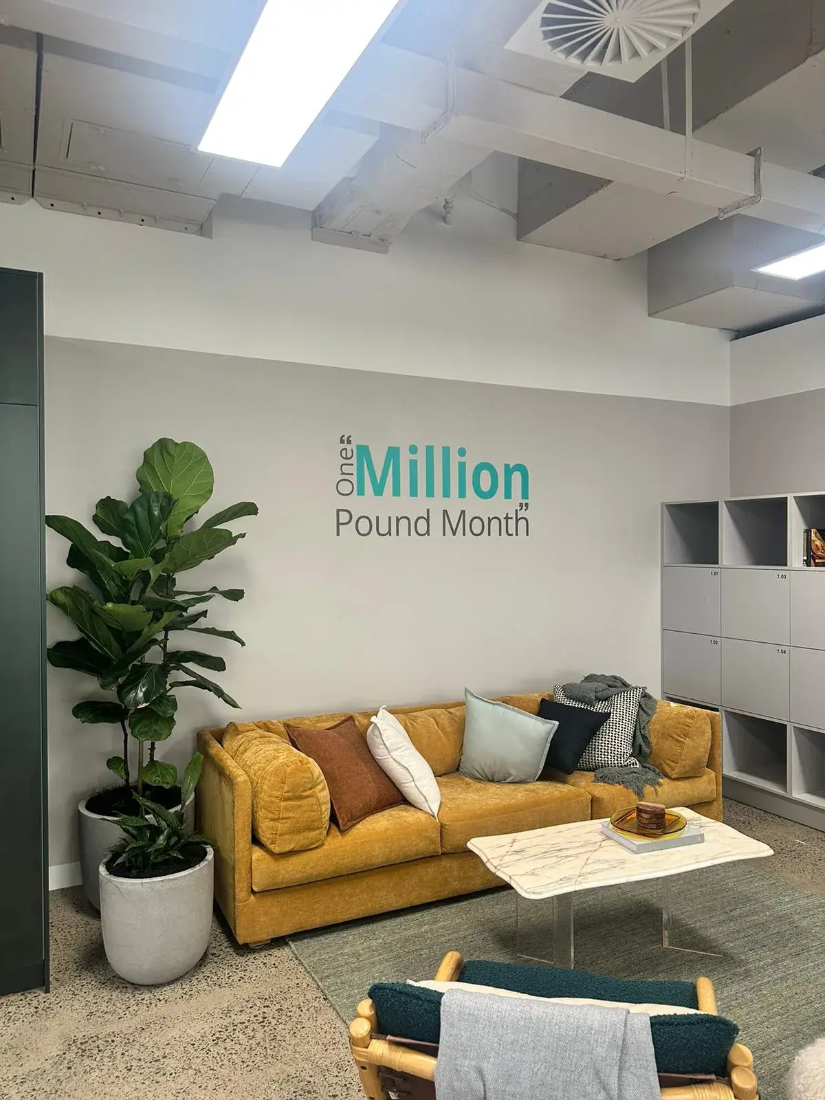 Matte wall graphic reading One Million Pound Month above a yellow sofa in the Alpha office
