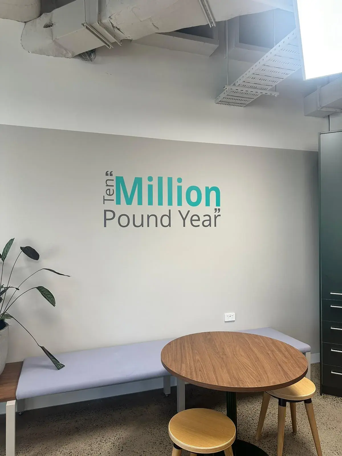 Matte wall graphic reading Ten Million Pound Year in an Alpha office breakout area
