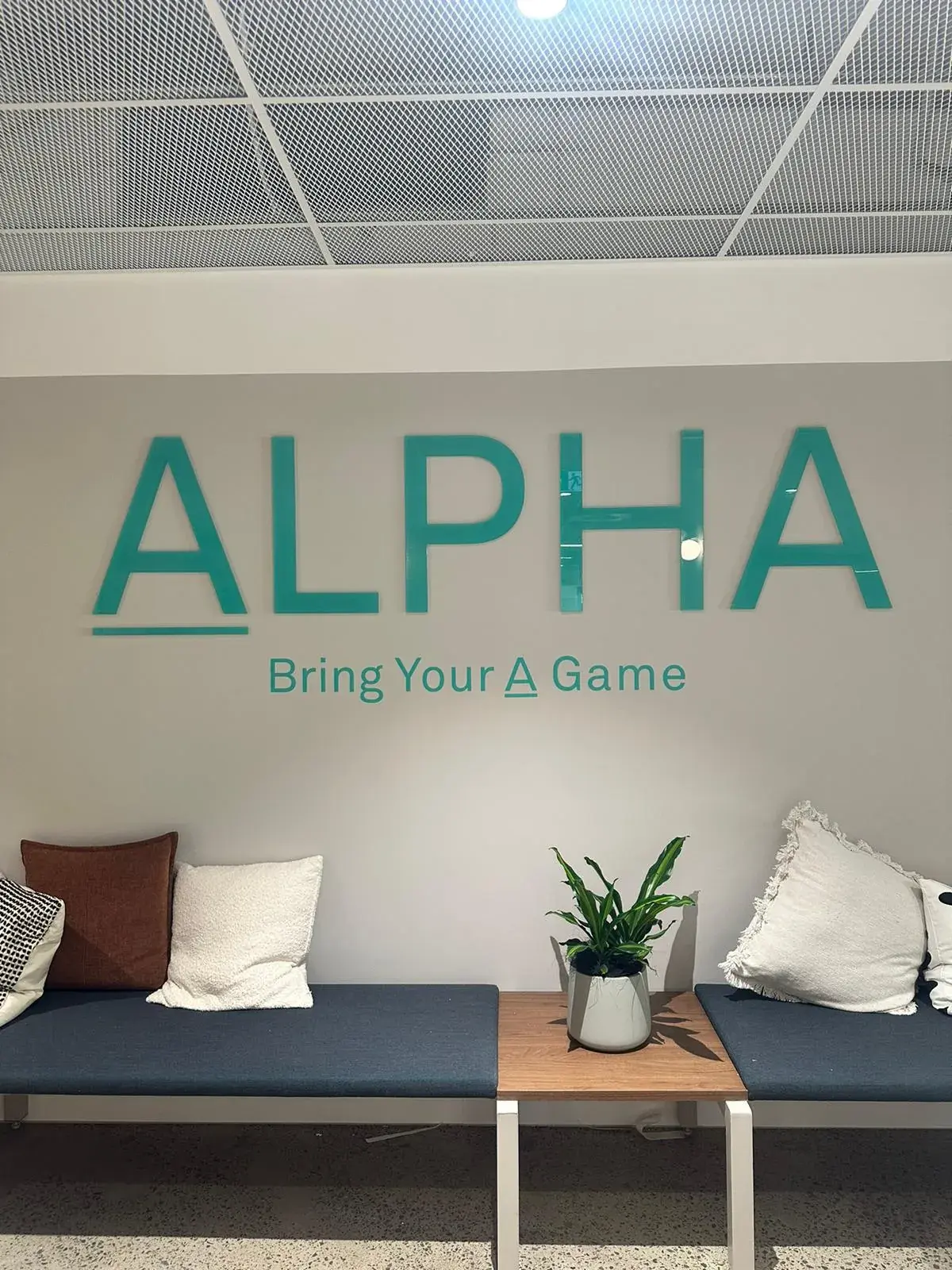 Close view of the turquoise Alpha wall logo and Bring Your A Game tagline above lounge seating