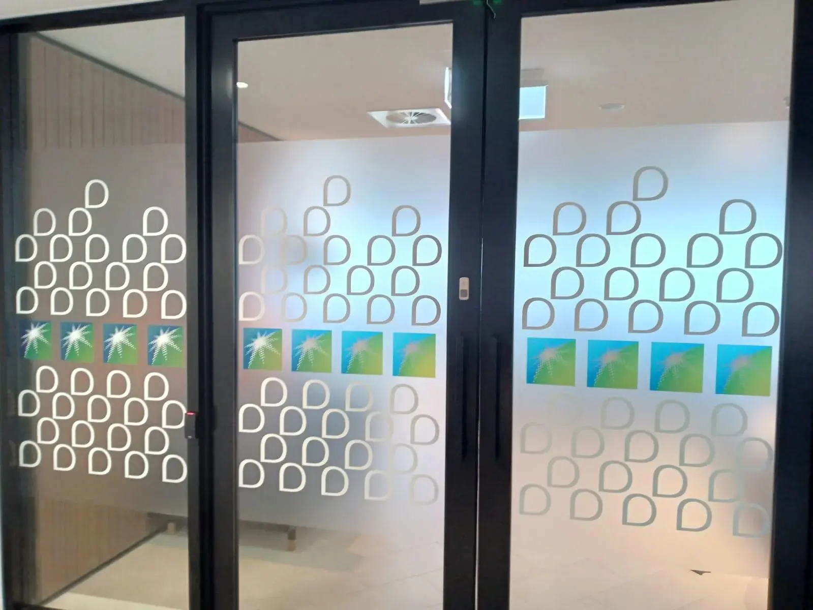 White printed privacy graphics and colour panels aligned across black-framed Aramco glass doors