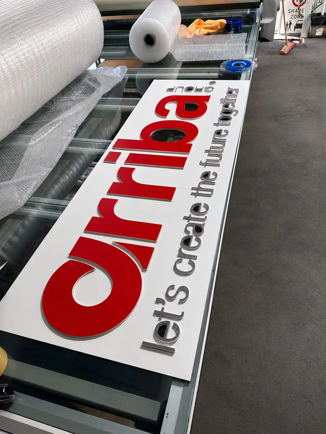 The finished Arriba Group reception lock-up face-up on the bench in our Sydney workshop, the red dimensional letters and grey tagline set onto the white panel with bubble wrap ready for packing