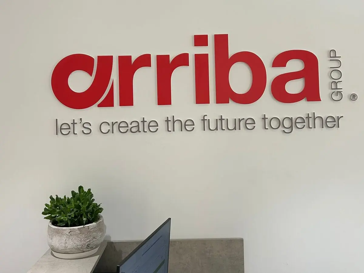 The finished Arriba Group reception lock-up installed on the white reception wall, the red dimensional letters and grey tagline reading let's create the future together above a potted plant on the reception desk in the Sydney office