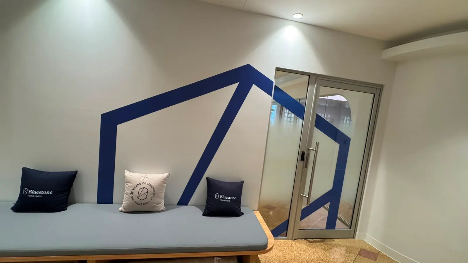 Large navy Bluestone brand graphic continuing from a painted plaster wall across a door frame and onto the glazed door beside a bench seat