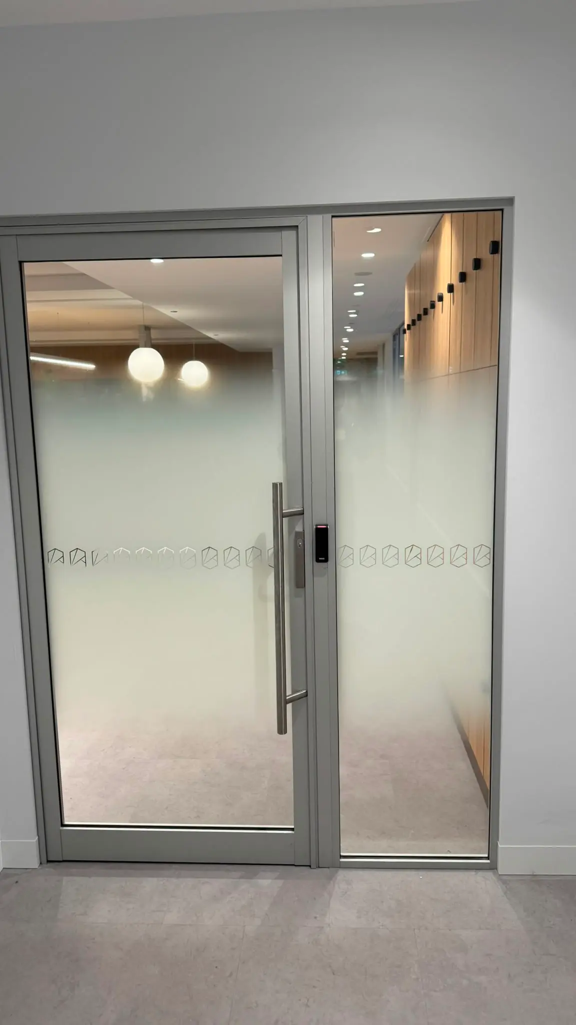 Aluminium framed glass entry door and sidelight carrying dense gradient film at the base with a hexagon icon band at handle height