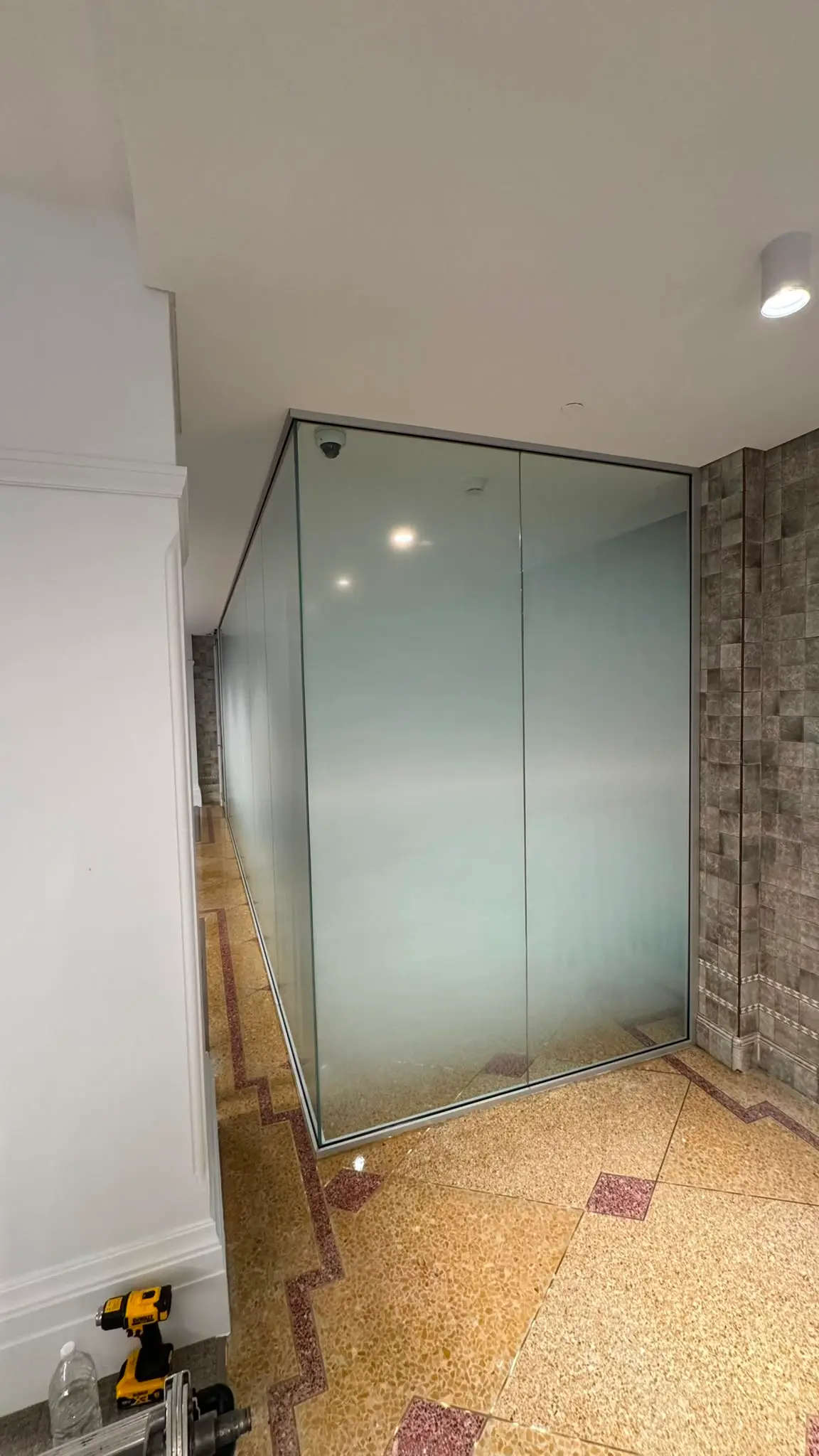 Full height glazed partition run carrying gradient film, wrapping a corner and receding down a corridor with install tools on the floor