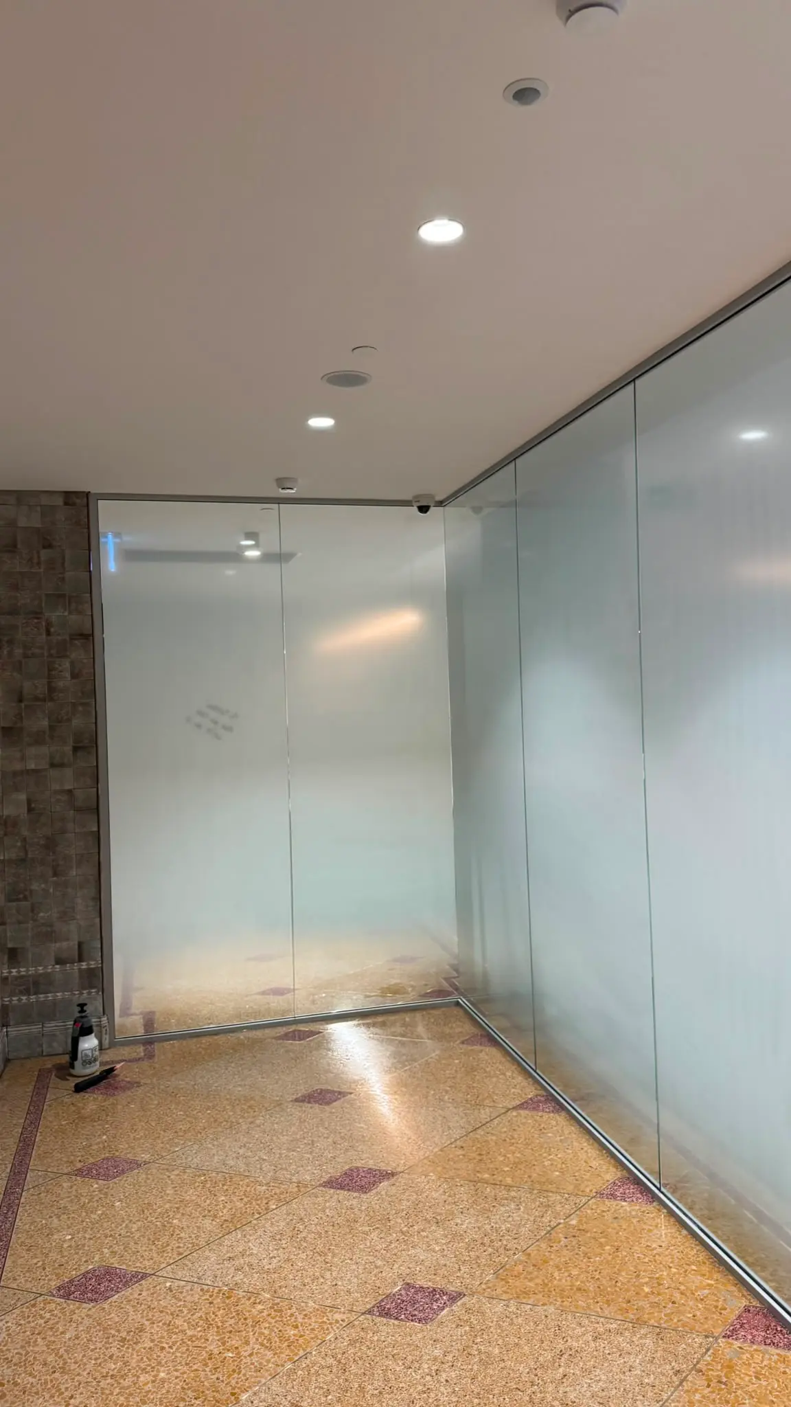 Corner return of the frosted glazing with a spray bottle and applicator on the floor beside a tiled feature wall during installation