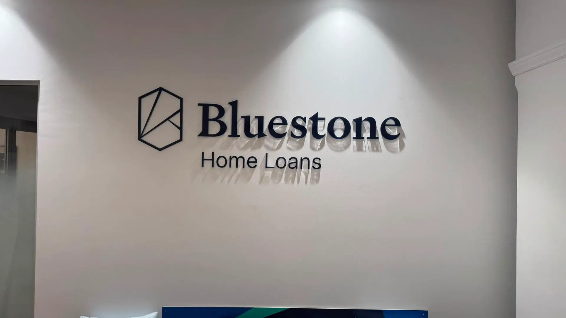 Bluestone Home Loans dimensional navy lettering and hexagonal logo mark on a white reception wall under a downlight