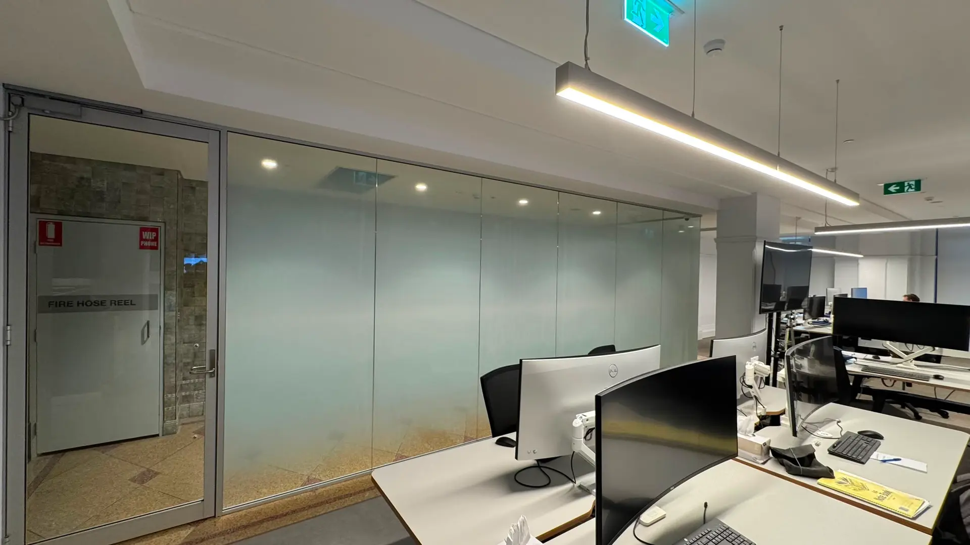 Long glazed partition run photographed from the workstation side, the printed gradient densest at floor level and clearing towards the ceiling above the desks