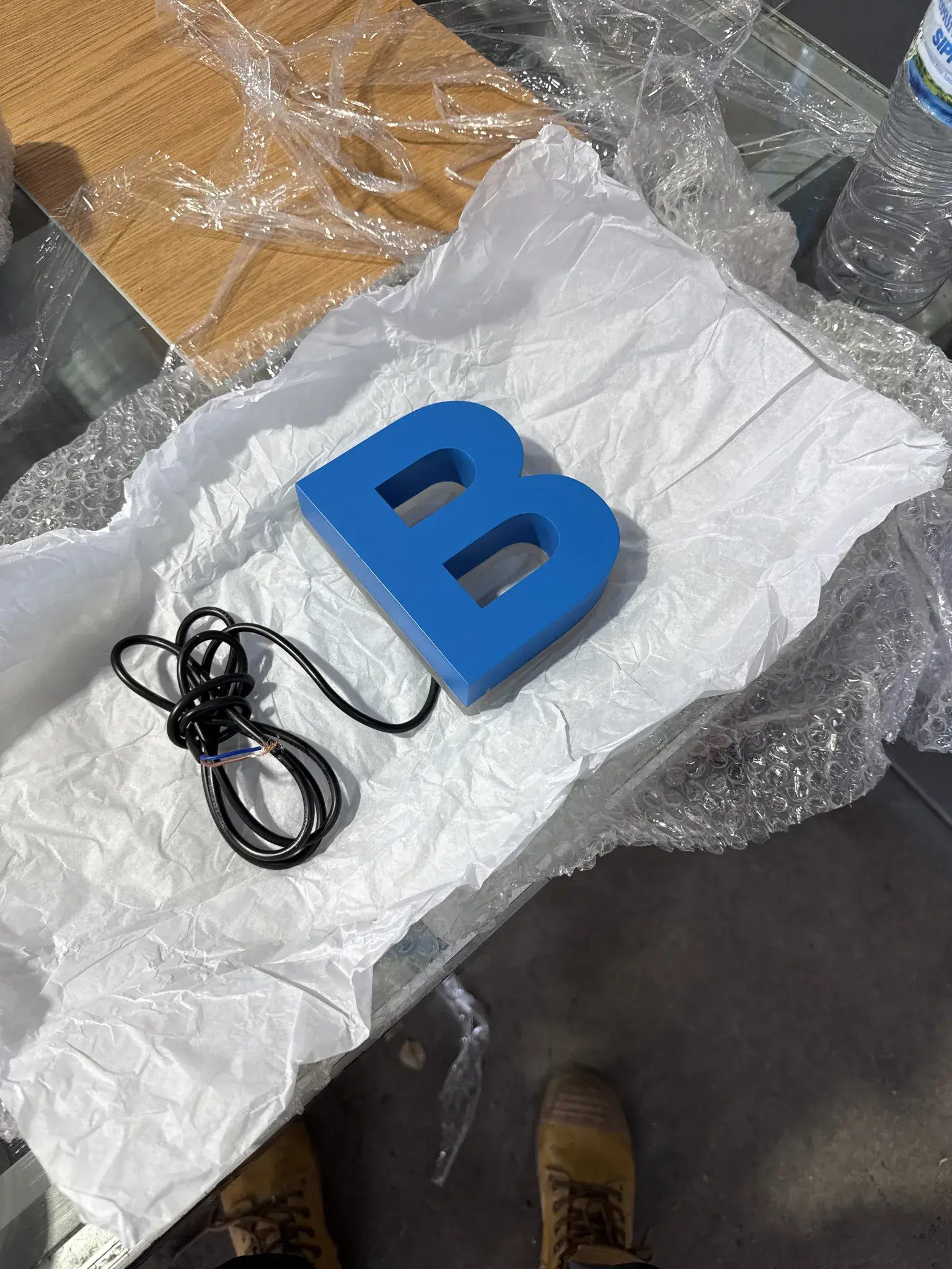 Fabricated blue BYRONS letter component prepared for illumination quality control and packing