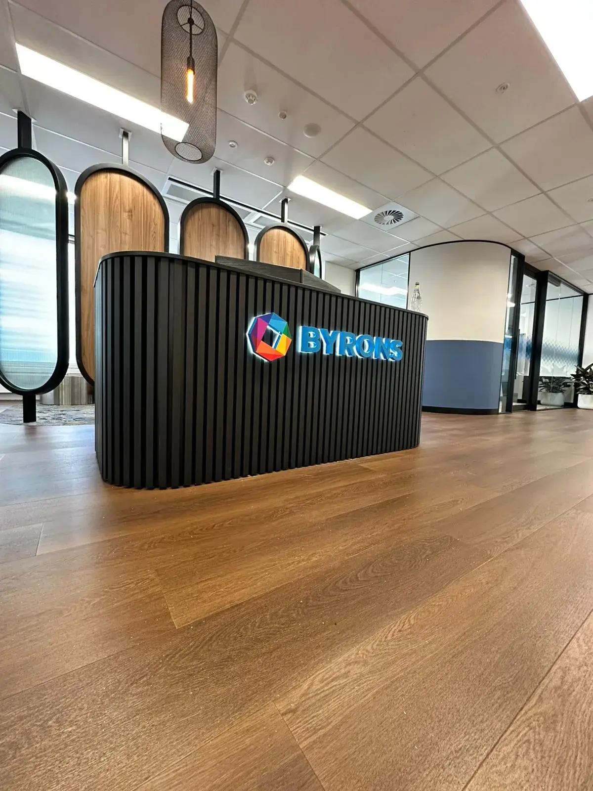 Oblique office view of the illuminated BYRONS emblem and lettering installed on the ribbed reception counter