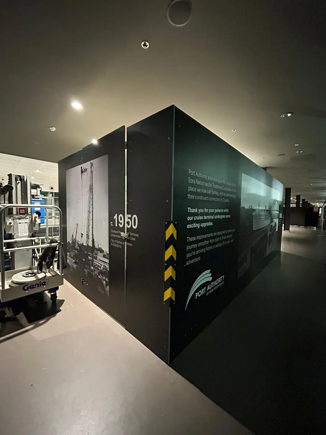 Low-lit interior hoarding run printed with a 1950 archival photograph, with a lift parked alongside during install