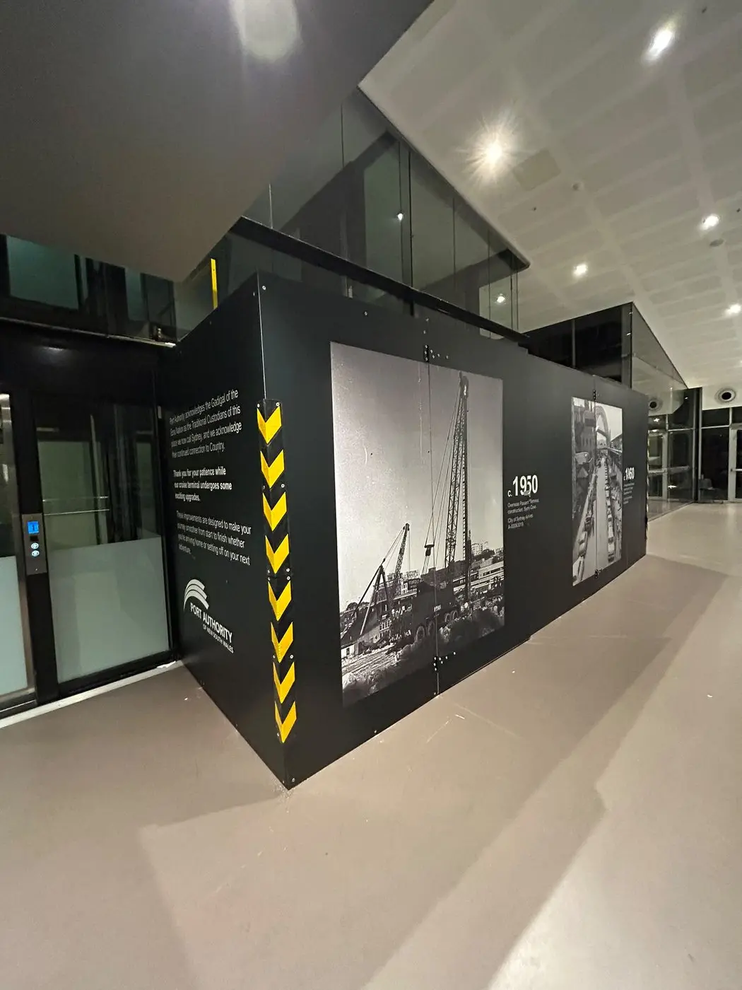 Interior hoarding with a 1950 archival construction photograph and yellow chevron markings wrapping the corner