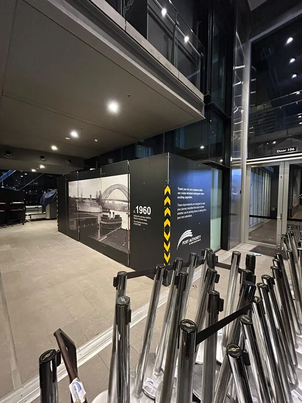 Interior hoarding printed with a 1960 archival photograph of the Harbour Bridge, seen past chrome queue stanchions