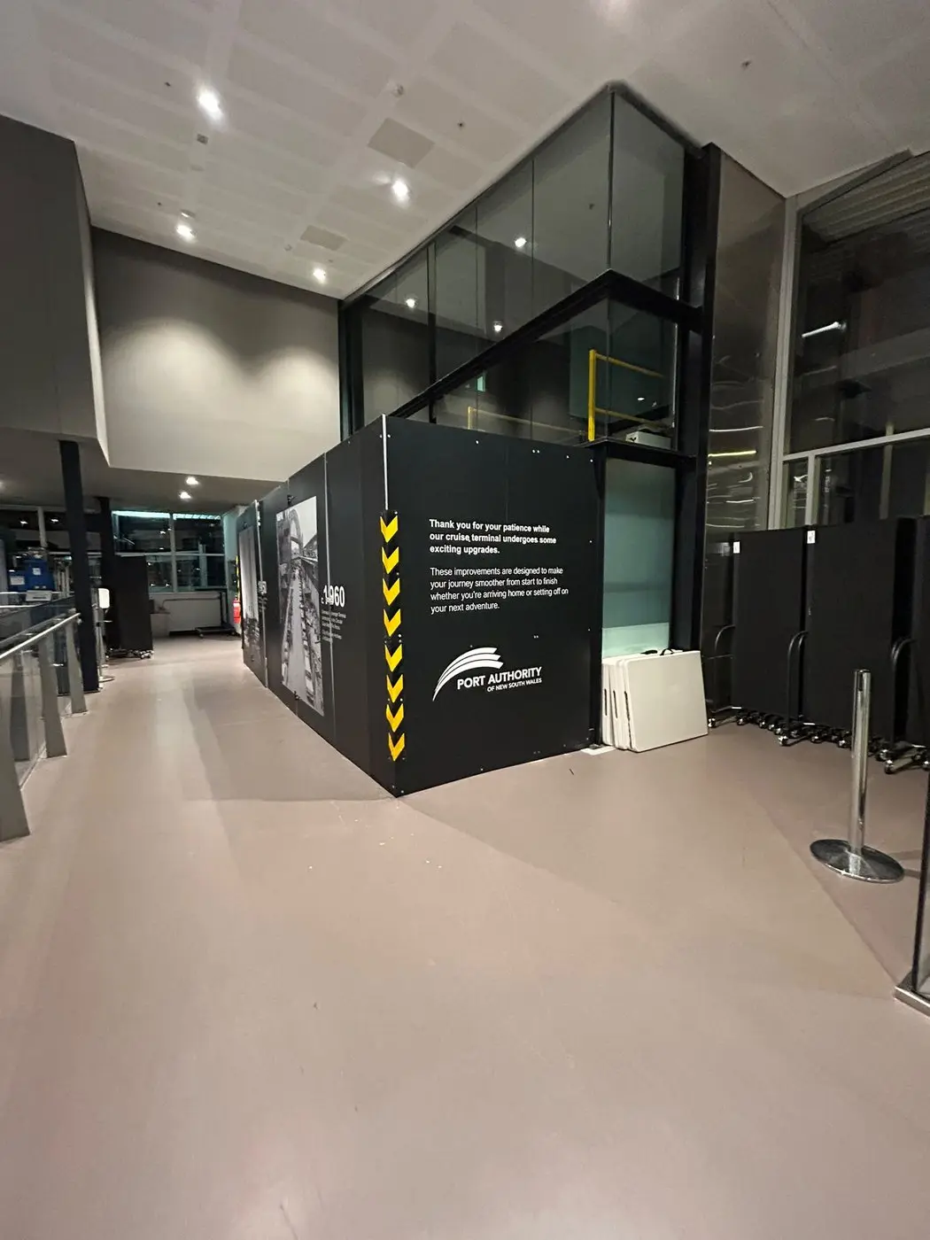 Hoarding wrapped around an internal corner beside the glass lift shaft, carrying the asset owner's passenger message