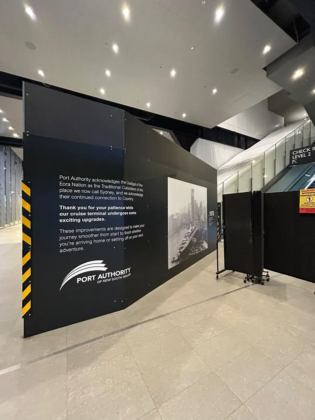 Interior hoarding panel printed with a harbour skyline photograph, installed on the passenger route to check-in