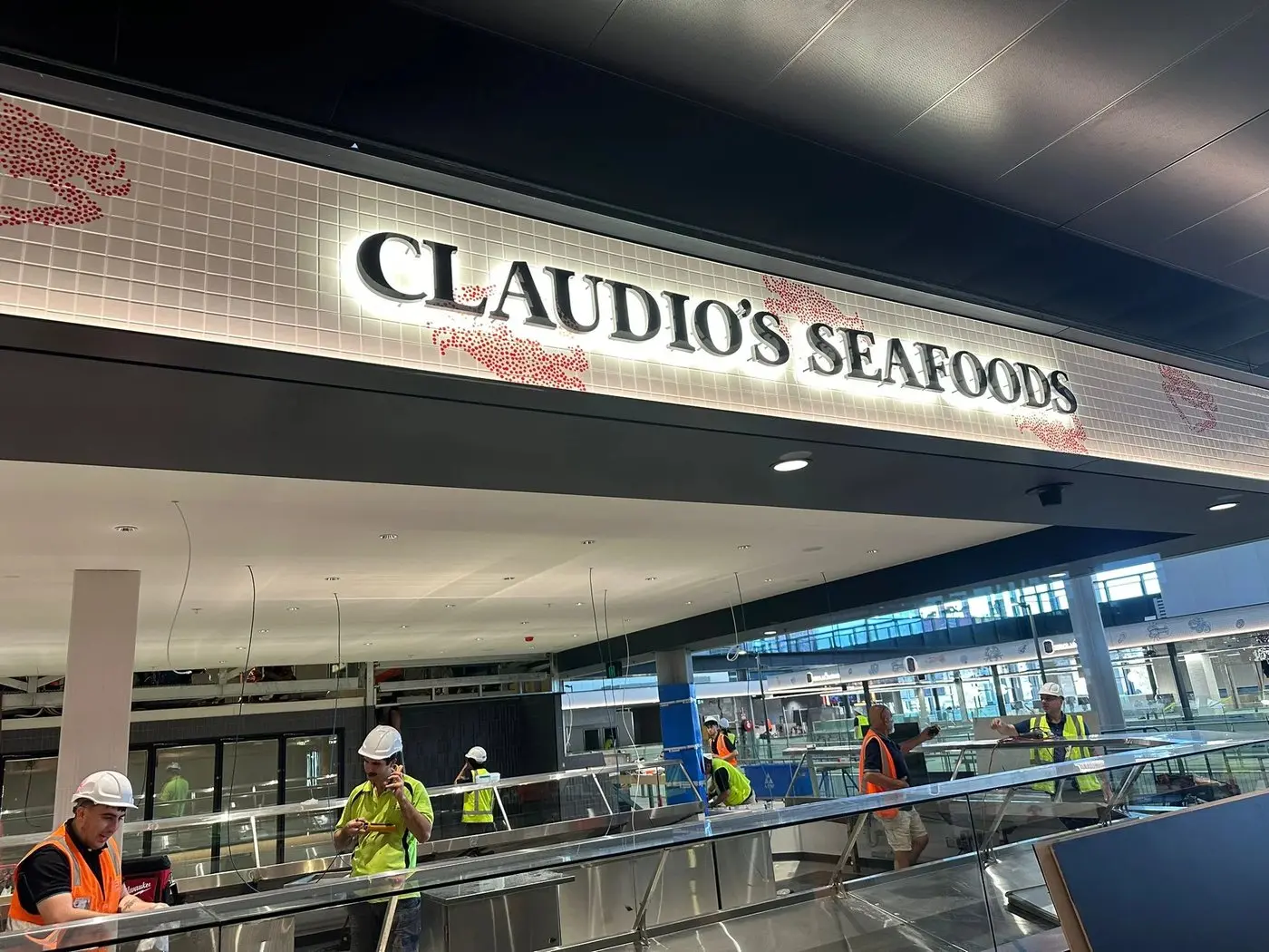 Claudio's Seafoods backlit dimensional letters glowing on the white mosaic bulkhead with red crab motifs at the new Sydney Fish Market