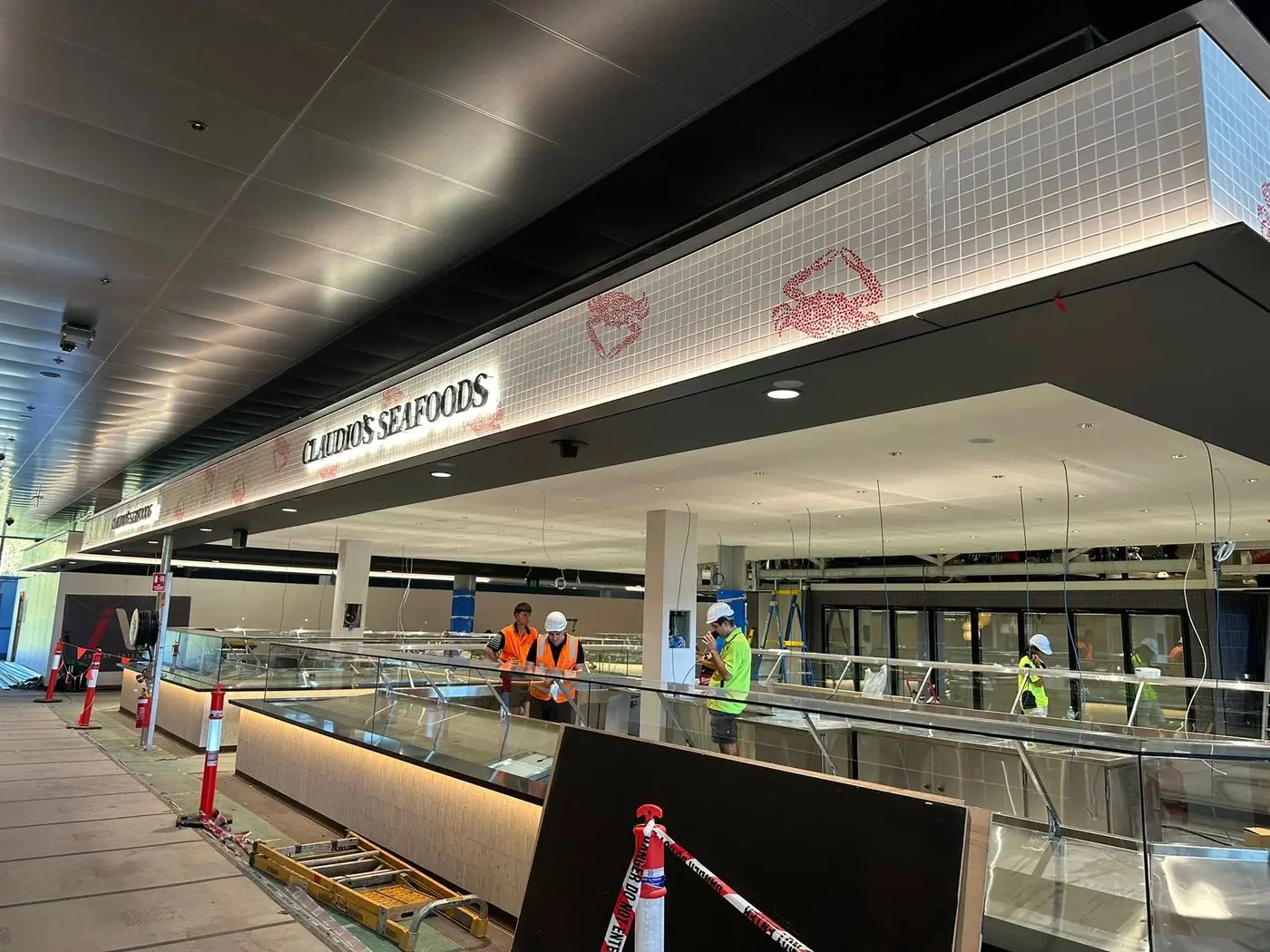 Wide view of the Claudio's Seafoods tenancy showing the crab-motif band and lettering wrapping multiple faces of the bulkhead