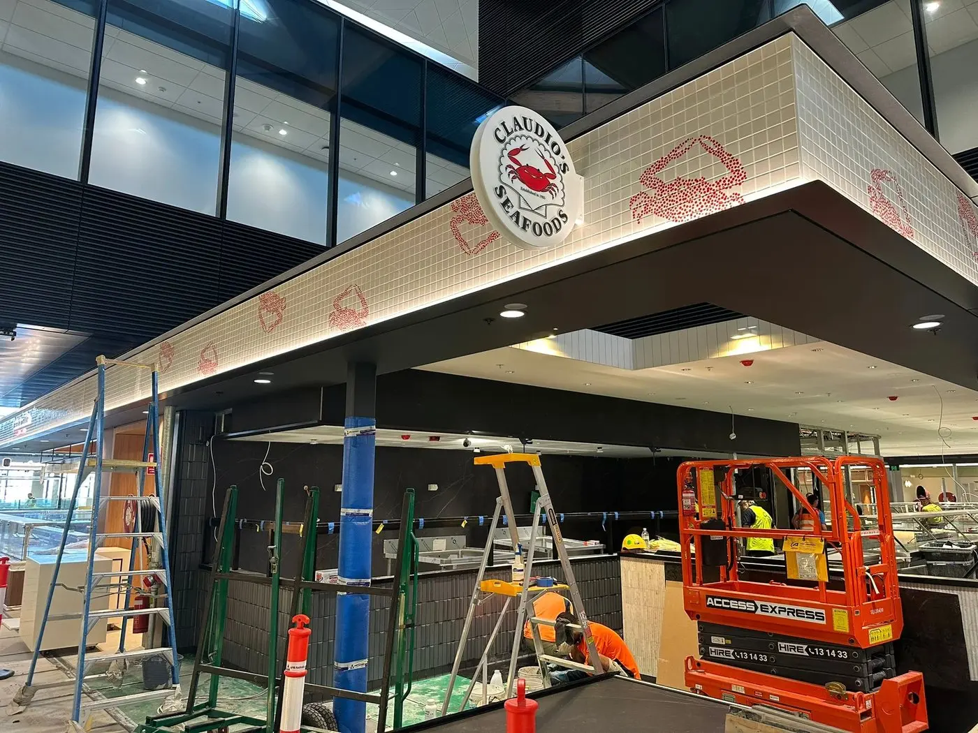 Corner of the tenancy with the round Claudio's Seafoods crab logo mounted on the bulkhead and scissor lifts working below