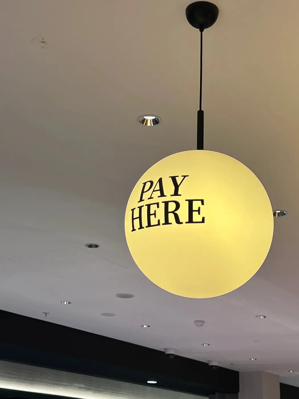 Spherical pendant light over the counter carrying applied Pay Here graphics