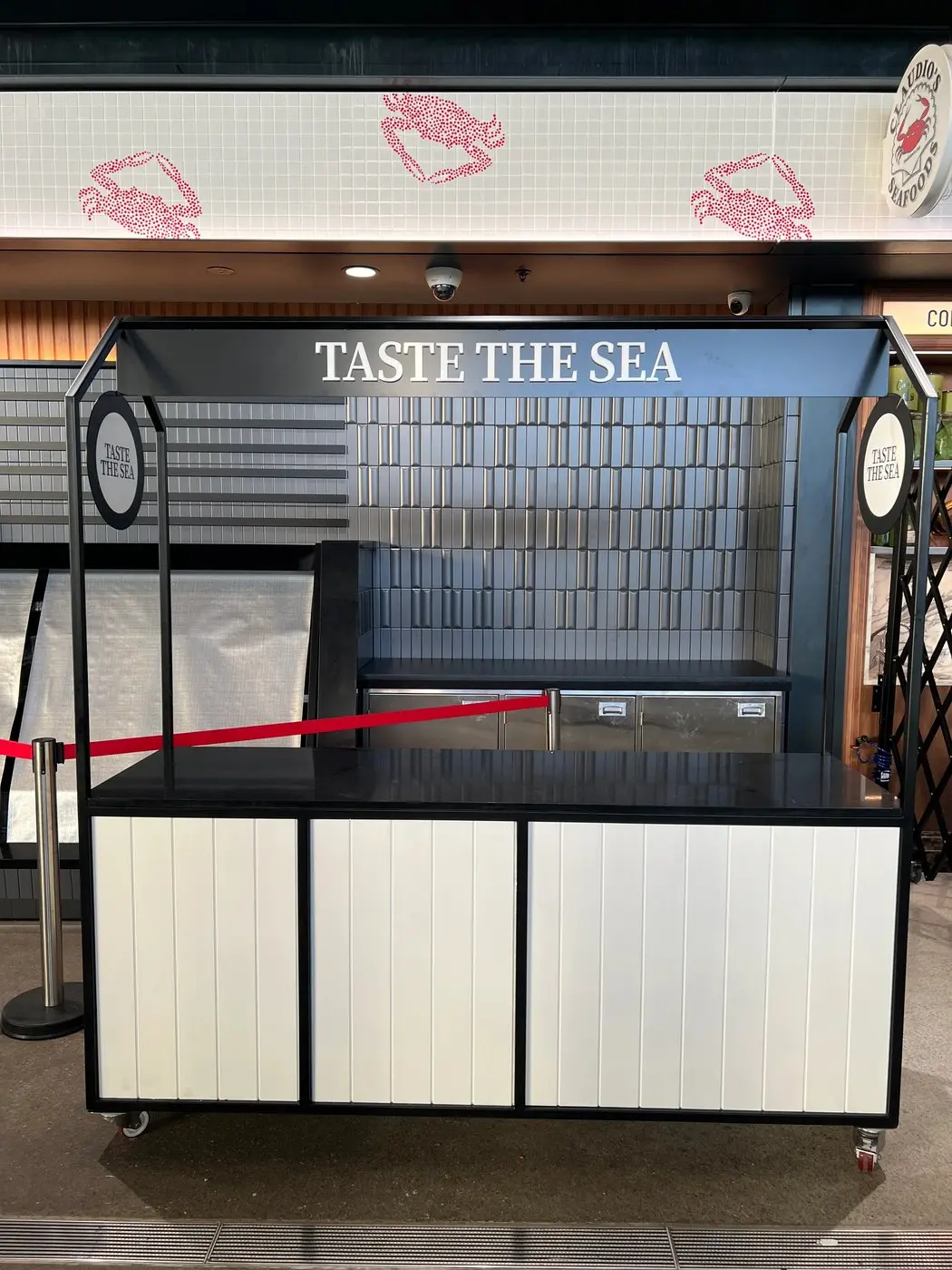 Mobile tasting cart with Taste the Sea header signage and Claudio's Seafoods branding in the market hall