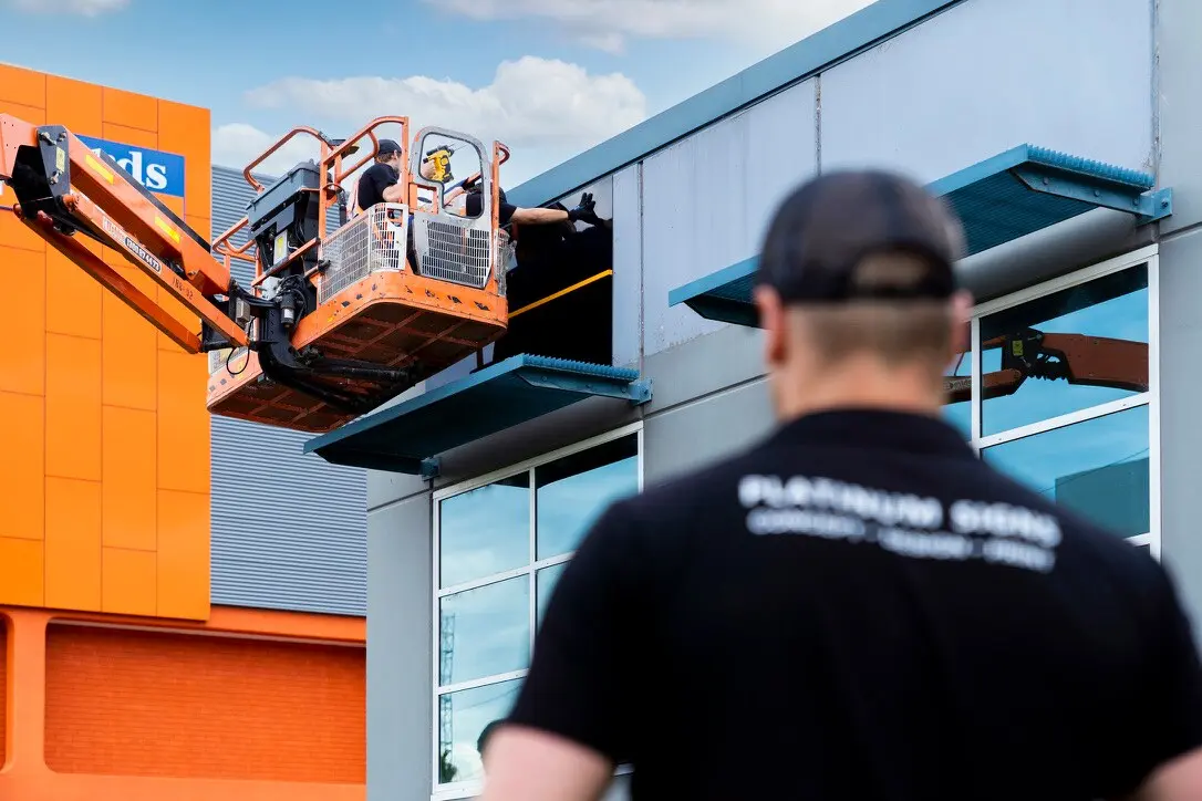 Boom-lift crew positioning the black ACM sign panel on the Sydney building façade