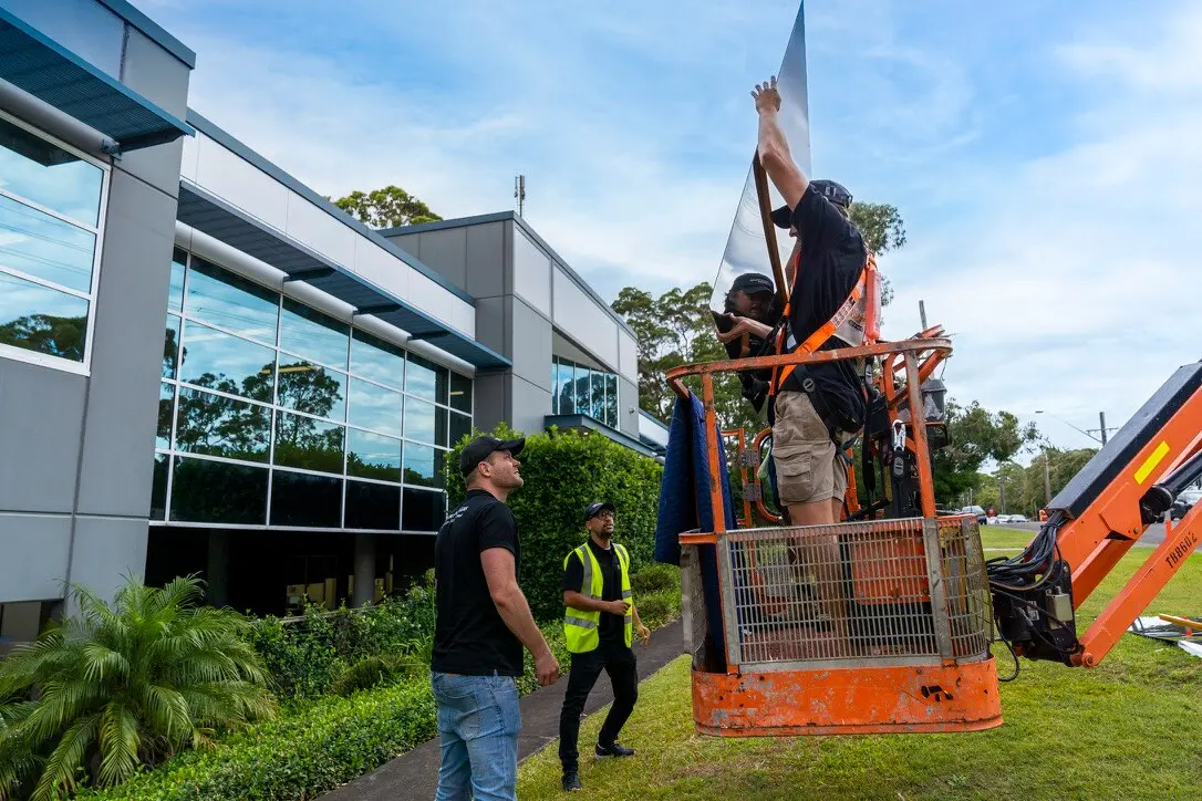 Installation crew guiding a large gloss-black ACM panel into the boom-lift basket