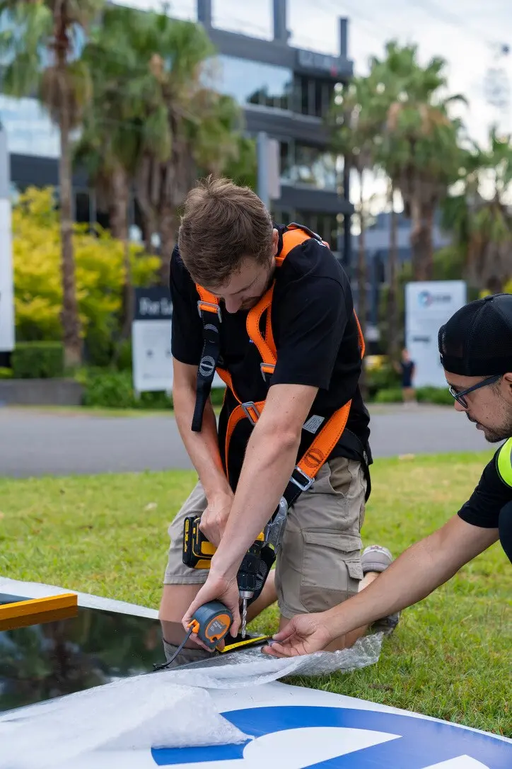 Two installers measuring and drilling the EDA ACM sign panel before it is lifted