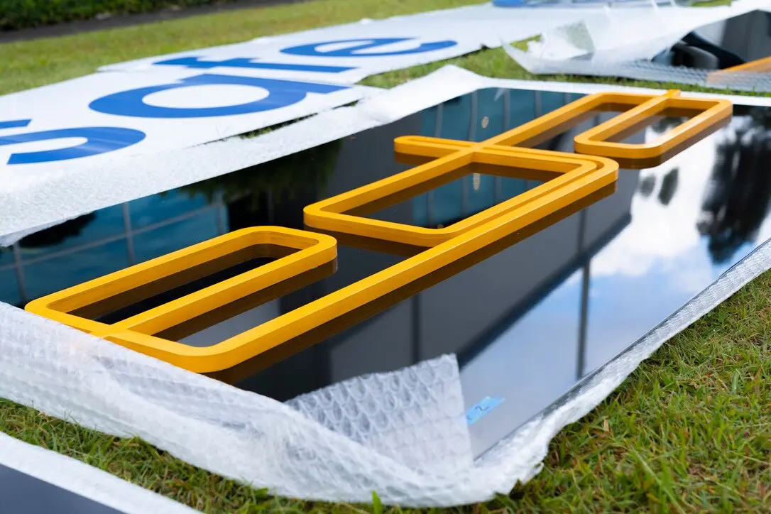 Yellow dimensional PVC EDA logo forms resting on a gloss-black ACM sign panel