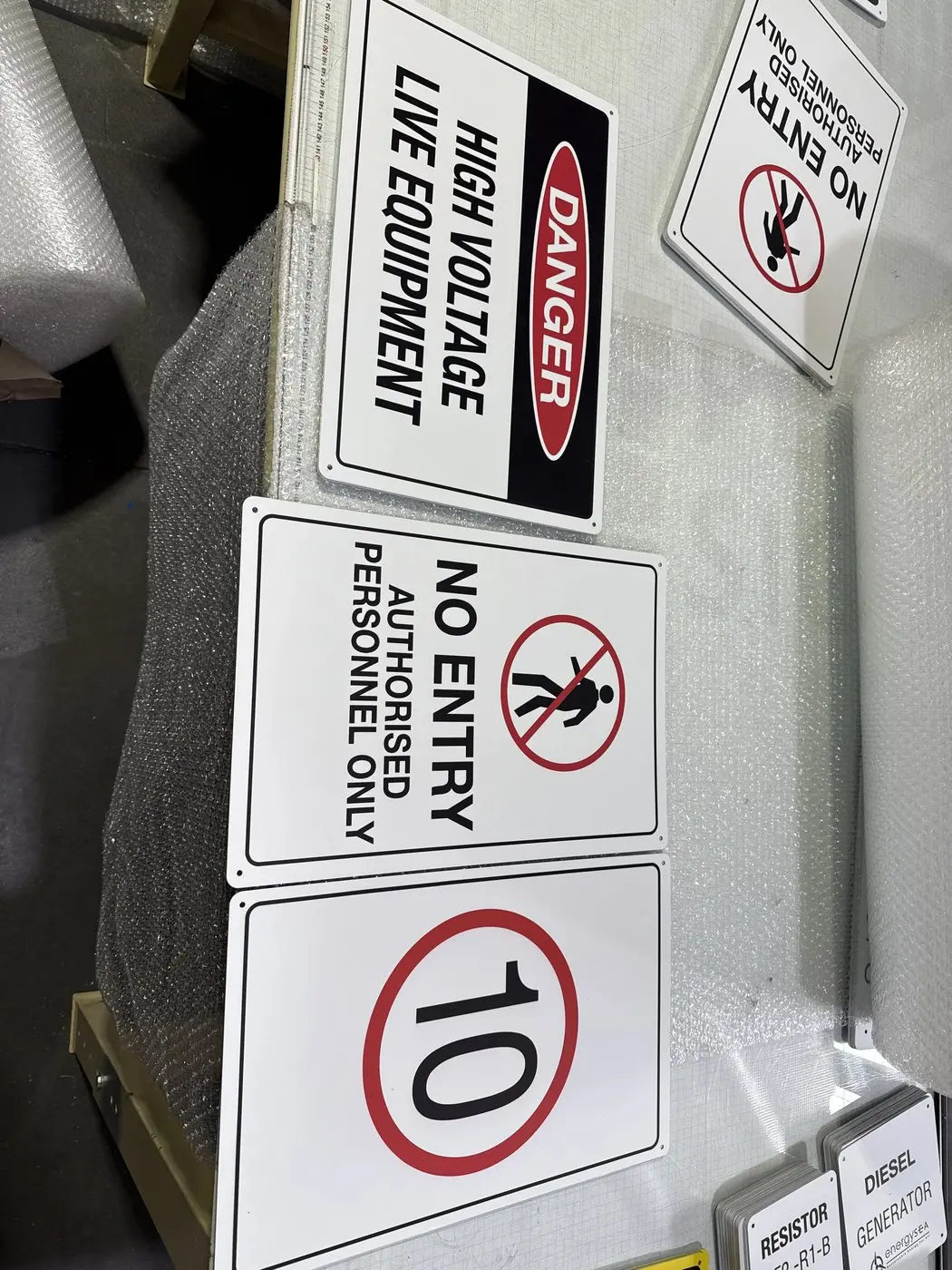 Stacks of finished substation safety signs of different types layered with protective wrap on the bench