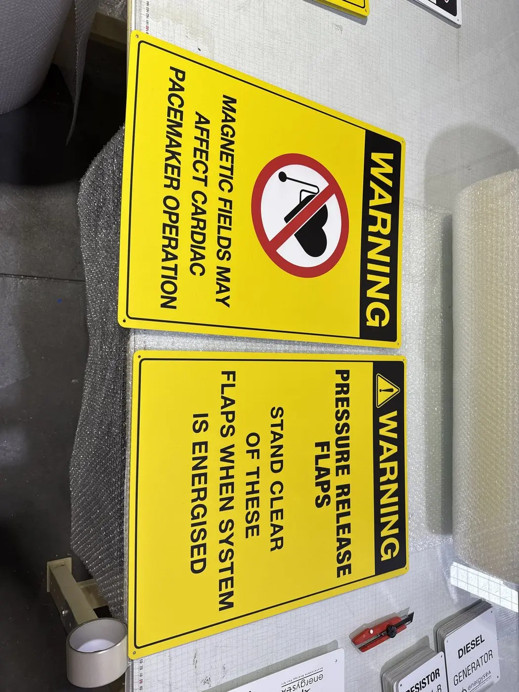 Pair of yellow warning signs covering pacemaker-affecting magnetic fields and pressure release flaps