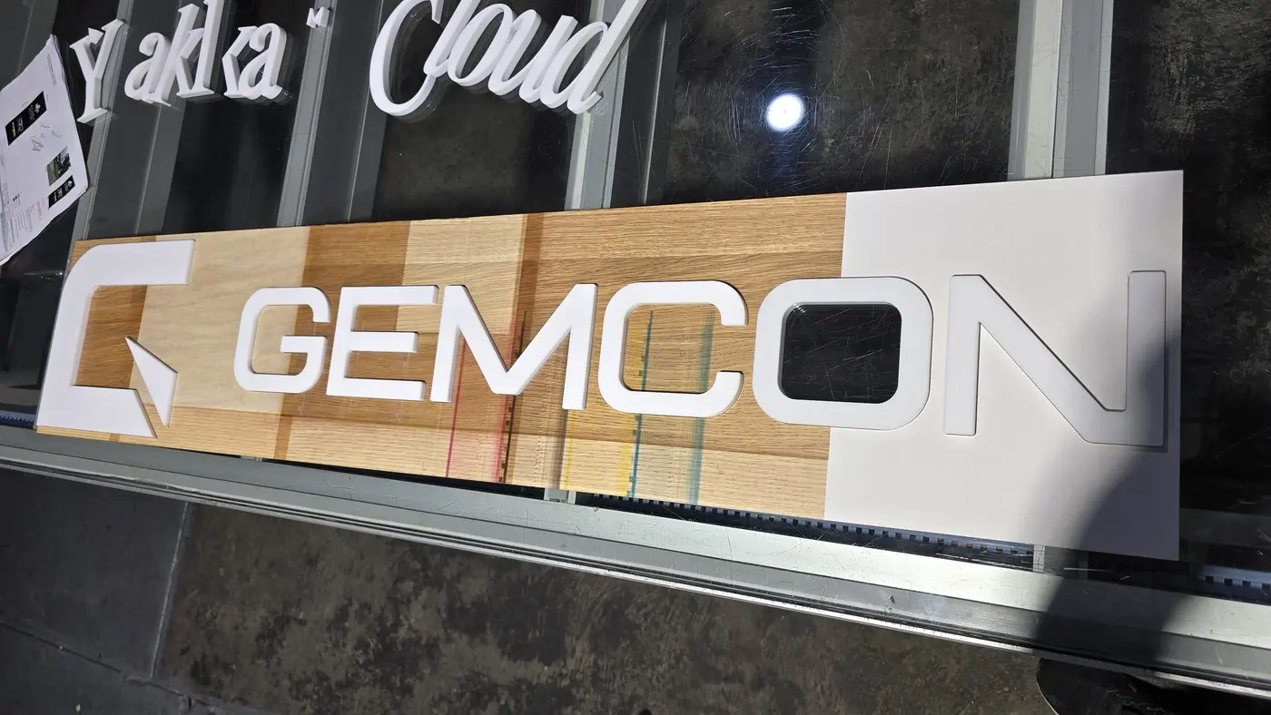 White dimensional GEMCON letters with a painted blue logo icon laid out on a timber-look board during the workshop build