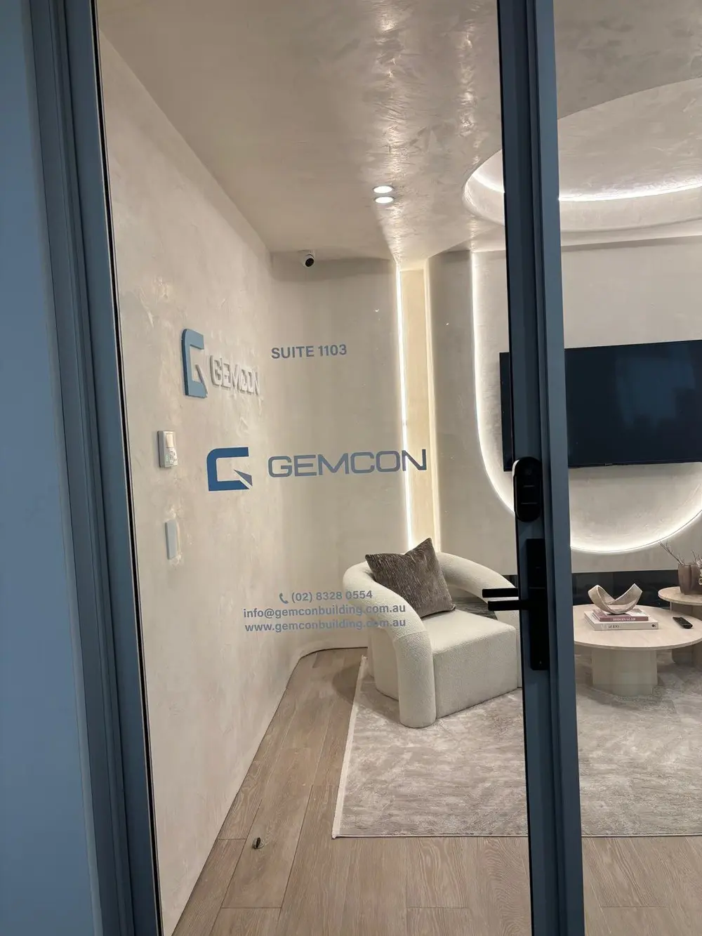 Glazed office front door carrying a digitally printed GEMCON logo and suite graphic, with the reception seating visible through the glass