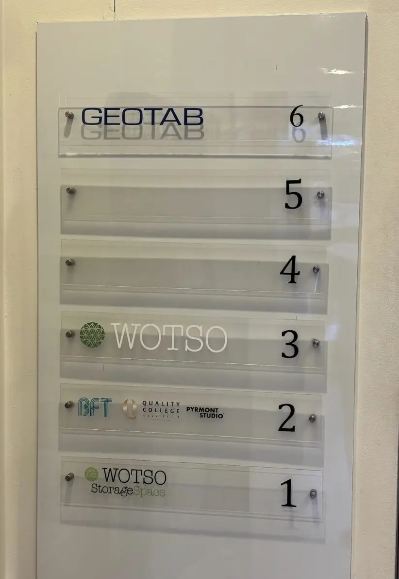 Shared building directory board with six numbered clear acrylic strips, the top strip carrying the Geotab name