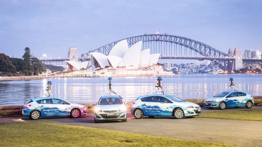 Four Google Street View vehicles with camera rigs lined up at dusk in front of the Sydney Opera House and Harbour Bridge
