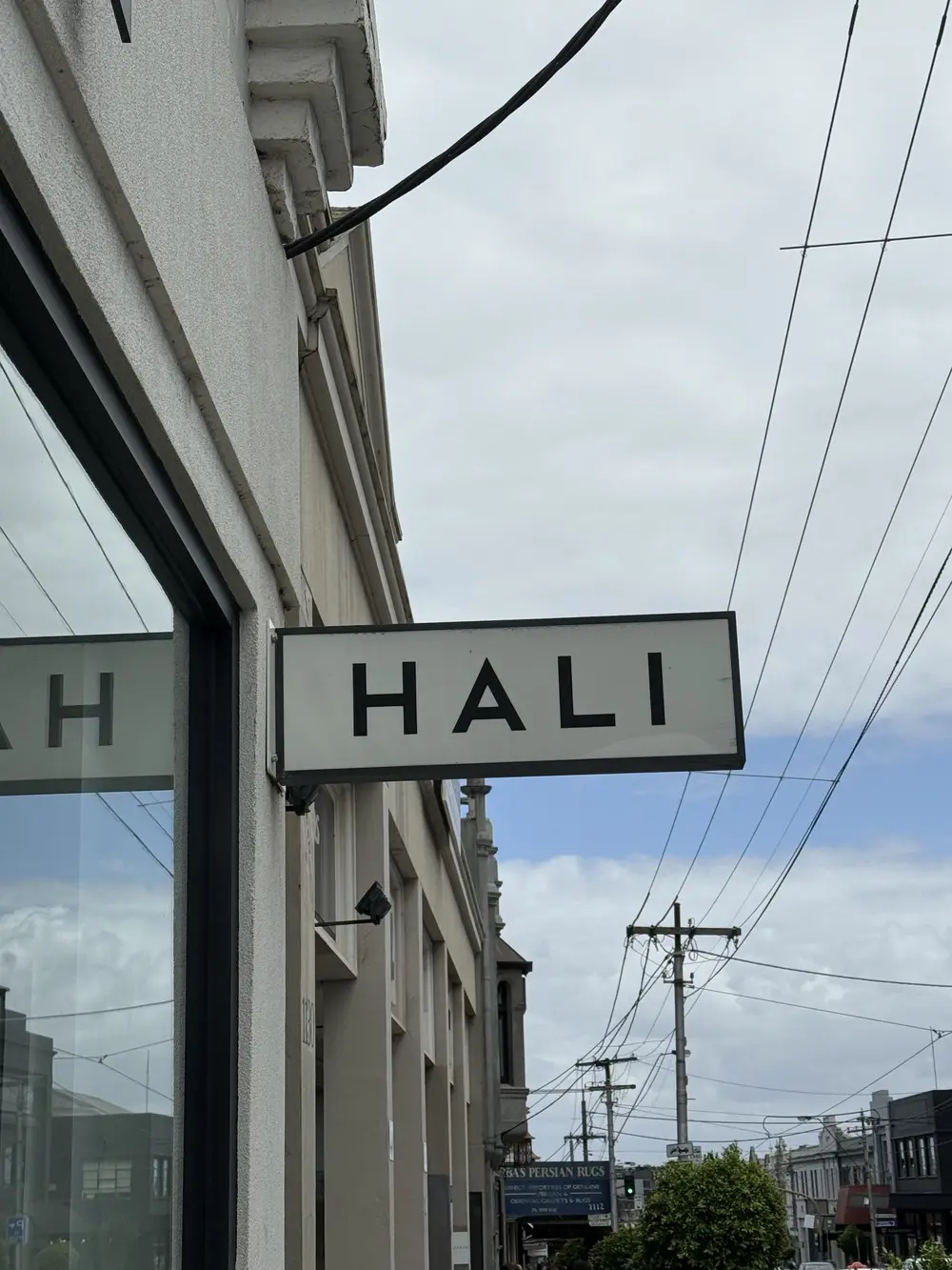 Rectangular double-sided LED light box carrying the HALI wordmark projecting from the shopfront awning over the footpath