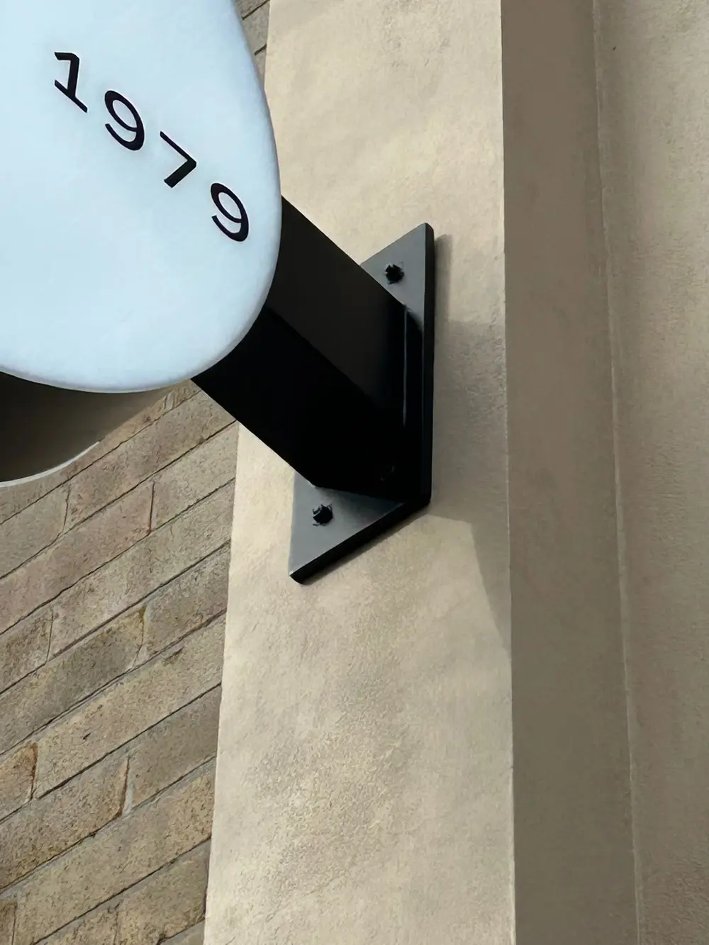 Close view of the black powder-coated wall plate and arm bracketing the round HALI light box off the rendered wall on visible fixings