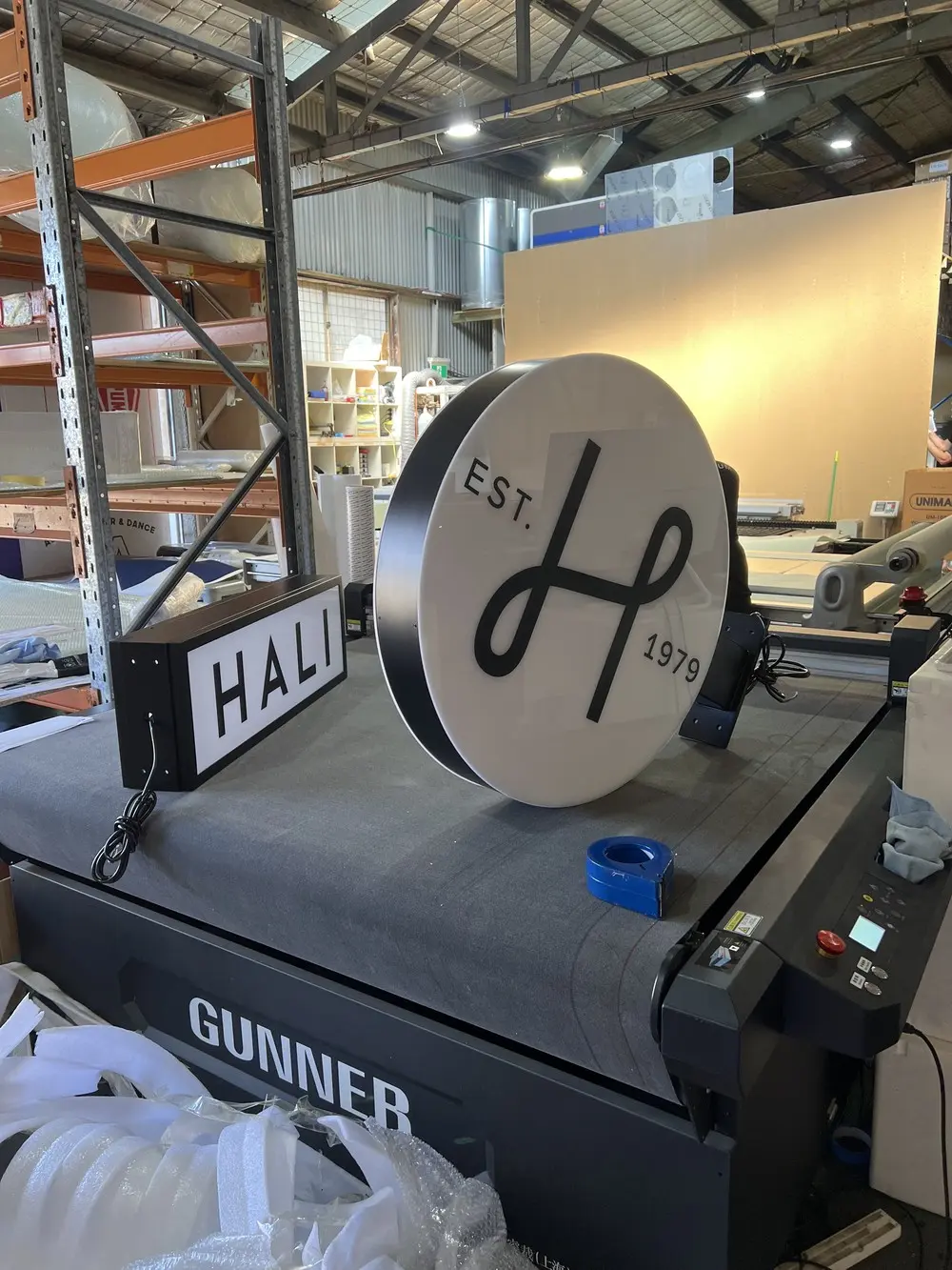 The round and rectangular HALI light boxes assembled and lit in the workshop beside a flatbed printer before installation