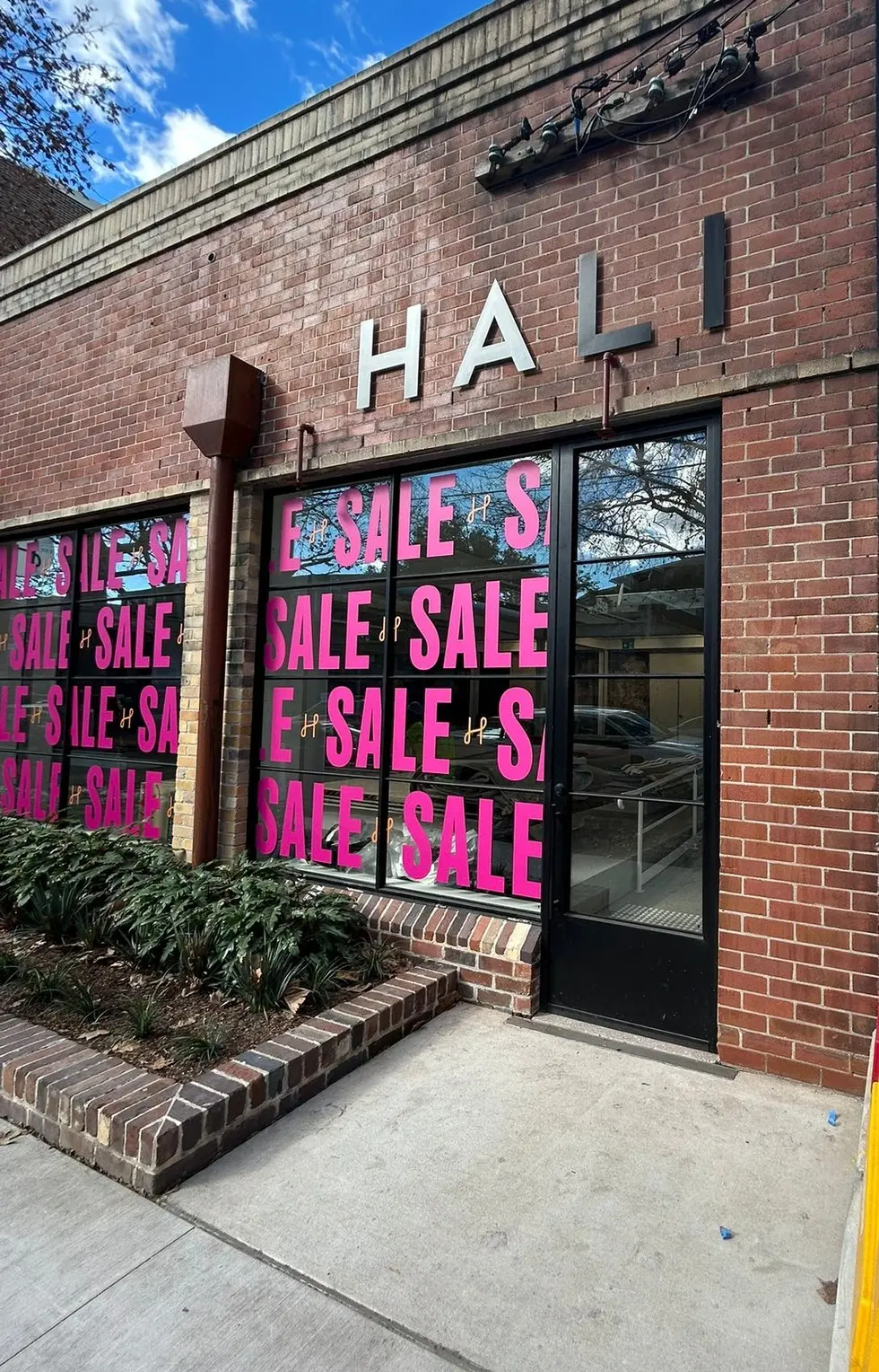 HALI brick shopfront with fabricated metal facade letters above bays of glazing carrying a repeating printed SALE window graphic