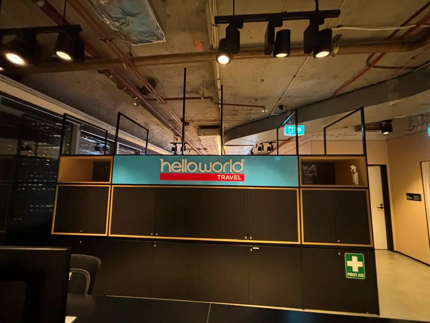 Blue helloworld Travel face-lit sign mounted above the dark reception joinery during the office fit-out