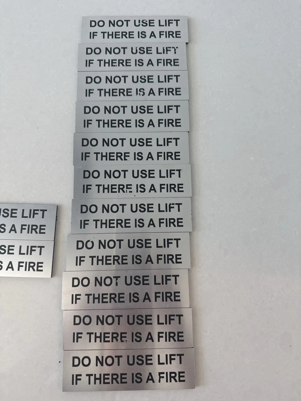 A batch of finished silver Do Not Use Lift If There Is A Fire signs laid out after printing
