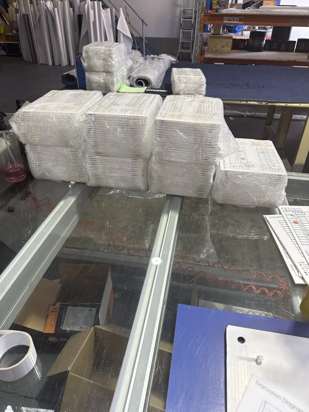 Stacks of wrapped acrylic evacuation diagram panels batched on the Platinum Signs workbench before delivery